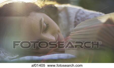 Stock Photography - Close up selective focus of sleeping woman laying in park grass napping and reading book. Fotosearch