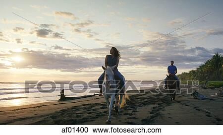 Couple riding horses on remote ocean beach under sunset sky View Large Photo Image Stock Image - Couple riding horses on remote ocean beach under sunset sky. Fotosearch