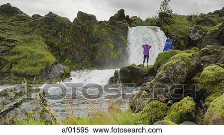 Couple standing on mossy boulders admiring waterfall river in rocky remote landscape View Large Photo Image Stock Photography - Couple standing on mossy boulders admiring waterfall river in rocky remote landscape. Fotosearch