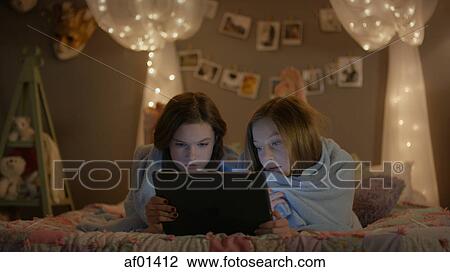 Curious teenage girls wrapped in blanket watching digital tablet on bed during sleepover View Large Photo Image Stock Image - Curious teenage girls wrapped in blanket watching digital tablet on bed during sleepover. Fotosearch