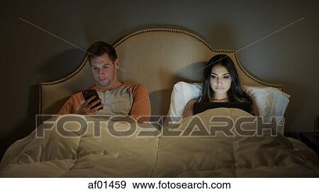 Distracted couple using laptop and cell phone separately in bedroom View Large Photo Image Stock Photo - Distracted couple using laptop and cell phone separately in bedroom. Fotosearch