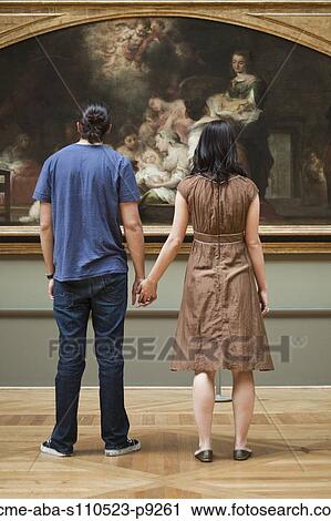 Stock Image - France, Paris, Young couple watching paintings in Louvre Museum. Fotosearch