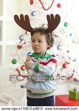Stock Image - Happy young boy deer horns standing in front of Christmas tree. Fotosearch