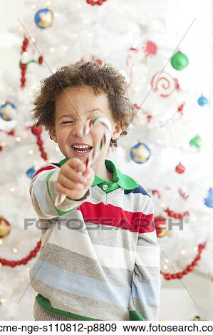 Stock Photo - Happy young boy with candy stick posing in front of Christmas tree. Fotosearch