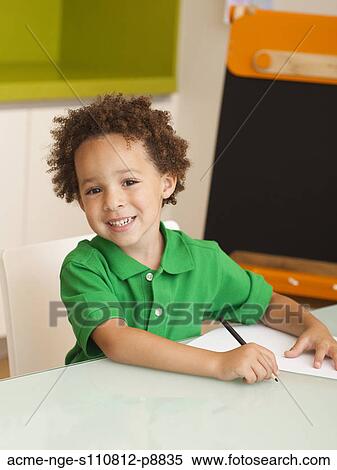 Stock Photography - Happy young boy writing on sheet of paper, blackboard in background. Fotosearch