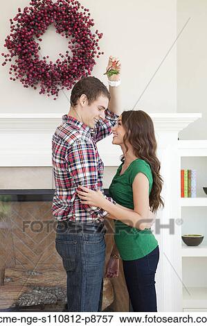 Stock Photo - Happy young couple embracing in front of fireplace with Christmas decoration. Fotosearch