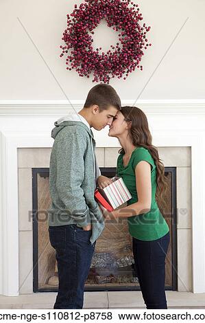 Stock Photo - Happy young couple kissing in front of fireplace, holding Christmas present. Fotosearch