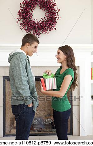 Stock Photo - Happy young couple standing in front of fireplace, holding Christmas present. Fotosearch