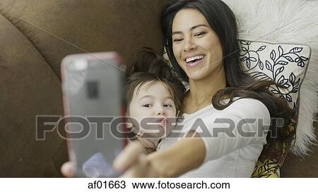 High angle selective focus view of playful mother and daughter posing and taking selfie with smartphone on sofa View Large Photo Image Stock Image - High angle selective focus view of playful mother and daughter posing and taking selfie with smartphone on sofa. Fotosearch