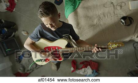 Picture - High angle view of intense teenage boy playing electric guitar in messy bedroom. Fotosearch