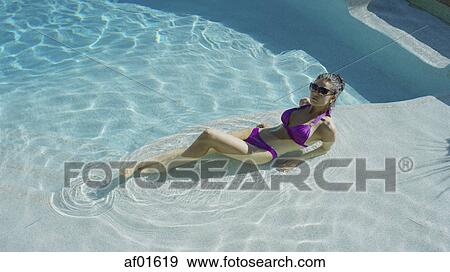 Stock Photo - High angle view of woman in bikini sunbathing and laying in swimming pool. Fotosearch