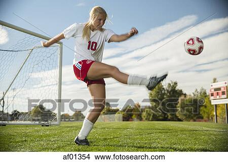 Low angle view of athlete kicking soccer ball on field under blue sky on sunny day View Large Photo Image Picture - Low angle view of athlete kicking soccer ball on field under blue sky on sunny day. Fotosearch