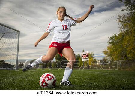Low angle view of athlete kicking soccer ball on field under cloudy sky View Large Photo Image Picture - Low angle view of athlete kicking soccer ball on field under cloudy sky. Fotosearch
