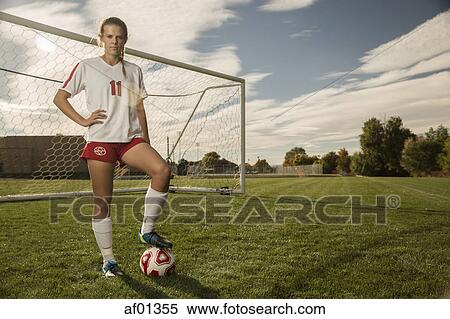 Stock Photography - Low angle view of athlete standing with soccer ball on field under blue sky on sunny day. Fotosearch