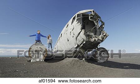 Low angle view of couple standing on airplane wreckage in remote landscape under blue sky View Large Photo Image Picture - Low angle view of couple standing on airplane wreckage in remote landscape under blue sky. Fotosearch