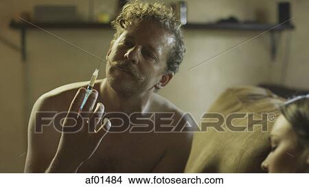 Picture - Low angle view of drug addict loading syringe needle for injection with tourniquet. Fotosearch