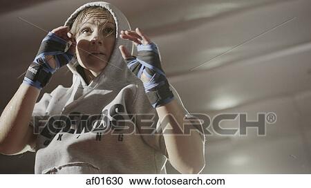 Stock Image - Low angle view of female boxer protecting her face standing in boxing ring during match. Fotosearch