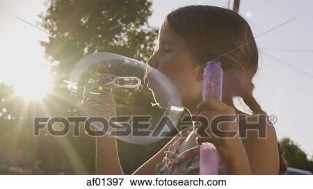 Low angle view of playful girl blowing bubble outdoors under sunset sky View Large Photo Image Stock Photo - Low angle view of playful girl blowing bubble outdoors under sunset sky. Fotosearch