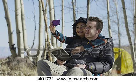 Low angle view of smiling couple hugging and posing for smartphone selfie in autumn woods View Large Photo Image Stock Image - Low angle view of smiling couple hugging and posing for smartphone selfie in autumn woods. Fotosearch