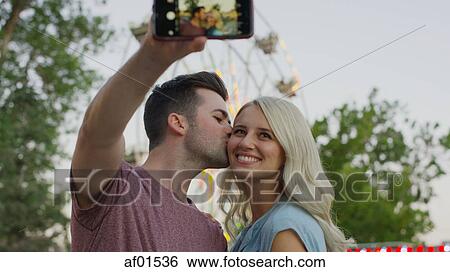 Low angle view of smiling couple kissing and taking selfie with smartphone camera outdoors View Large Photo Image Stock Photograph - Low angle view of smiling couple kissing and taking selfie with smartphone camera outdoors. Fotosearch