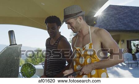Stock Image - Low angle view of smiling men cooking barbecue food on grill in sunny backyard. Fotosearch
