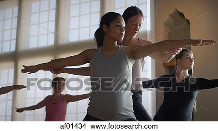 Low angle view of teacher adjusting woman's pose in yoga class View Large Photo Image Picture - Low angle view of teacher adjusting woman's pose in yoga class. Fotosearch