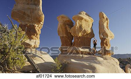 Picture - Low angle view of woman practicing yoga and meditating on rock formations in remote desert landscape under clear blue sky. Fotosearch