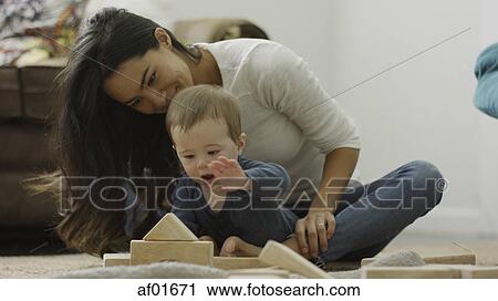 Stock Image - Mother and curious baby son sitting on floor and playing with building blocks. Fotosearch