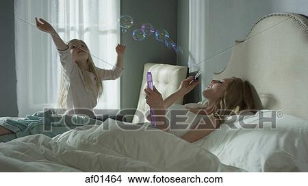 Mother and daughter playing and blowing bubbles in bedroom View Large Photo Image Picture - Mother and daughter playing and blowing bubbles in bedroom. Fotosearch