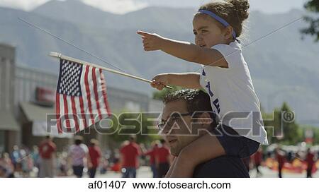 Stock Photo - Patriotic father carrying daughter on shoulder and waving American flag at parade. Fotosearch