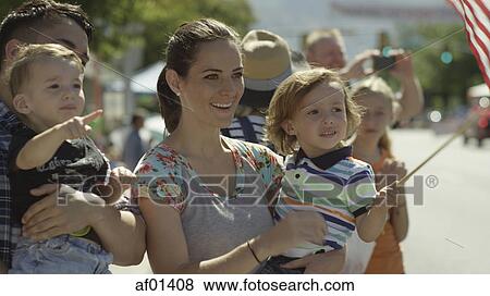 Stock Photo - Patriotic mother carrying son and waving American flag at parade. Fotosearch