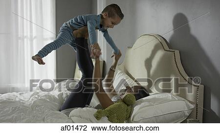 Playful mother lifting laughing son on bed View Large Photo Image Stock Image - Playful mother lifting laughing son on bed. Fotosearch
