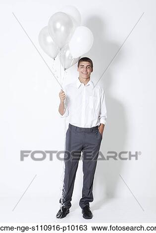 Stock Image - Portrait of young man holding balloons at party. Fotosearch