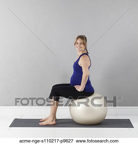 Stock Photo - Portrait of young pregnant woman sitting on fitness ball, studio shot. Fotosearch