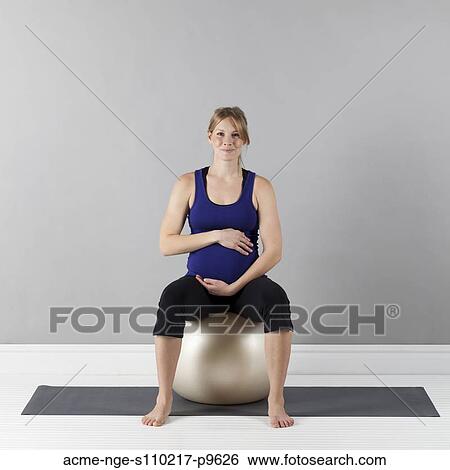Stock Photograph - Portrait of young pregnant woman sitting on fitness ball, studio shot. Fotosearch