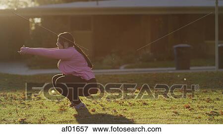 Stock Photo - Profile of backlit woman squatting and working out in sunny backyard. Fotosearch
