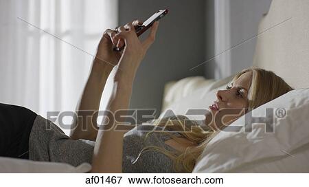 Profile of bored woman laying on bed using cell phone View Large Photo Image Stock Photo - Profile of bored woman laying on bed using cell phone. Fotosearch