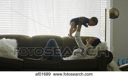 Profile of laughing playful mother baby son in mid-air and playing on sofa View Large Photo Image Stock Photo - Profile of laughing playful mother baby son in mid-air and playing on sofa. Fotosearch