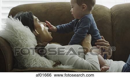 Profile of laughing playful mother holding baby son and playing on sofa View Large Photo Image Stock Photograph - Profile of laughing playful mother holding baby son and playing on sofa. Fotosearch