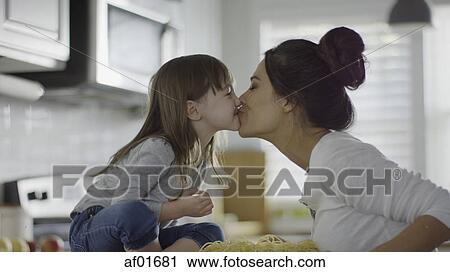 Stock Image - Profile of playful mother and daughter kissing over spaghetti pasta in kitchen. Fotosearch