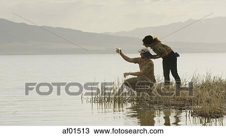 Stock Image - Profile of scientists working together and examining water sample in reeds at remote grassy lake shore. Fotosearch