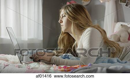 Profile of serious teenage girl using laptop in bed View Large Photo Image Stock Photograph - Profile of serious teenage girl using laptop in bed. Fotosearch