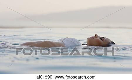 Profile of woman in bikini floating in infinity pool overlooking horizon and remote landscape View Large Photo Image Stock Image - Profile of woman in bikini floating in infinity pool overlooking horizon and remote landscape. Fotosearch
