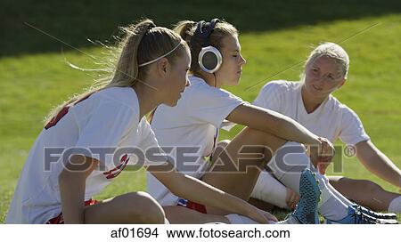 Profile view of athlete listening to headphones with teammate soccer players sitting on field View Large Photo Image Picture - Profile view of athlete listening to headphones with teammate soccer players sitting on field. Fotosearch