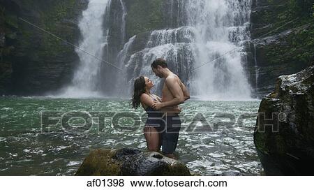 Romantic couple hugging in river under tropical waterfall View Large Photo Image Stock Photo - Romantic couple hugging in river under tropical waterfall. Fotosearch