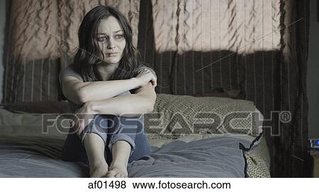 Sad battered woman holding her knees and crying on bed View Large Photo Image Stock Photo - Sad battered woman holding her knees and crying on bed. Fotosearch