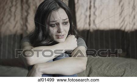 Sad battered woman holding her knees and crying on bed View Large Photo Image Stock Photo - Sad battered woman holding her knees and crying on bed. Fotosearch