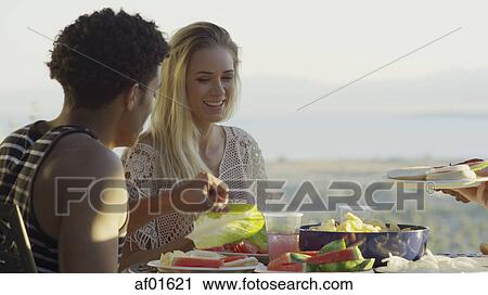Stock Image - Selective focus view of couple eating outdoors near scenic view of remote landscape. Fotosearch