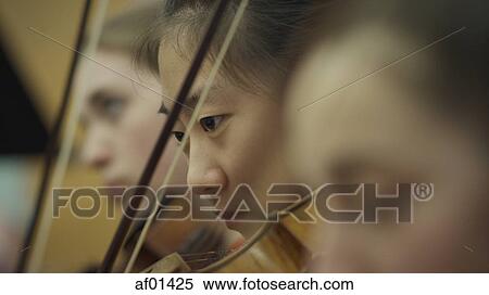 Stock Photography - Selective focus view of serious teenage girl musician playing violin in band class. Fotosearch