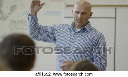 Stock Image - Selective focus view of teacher gesturing and talking in classroom. Fotosearch